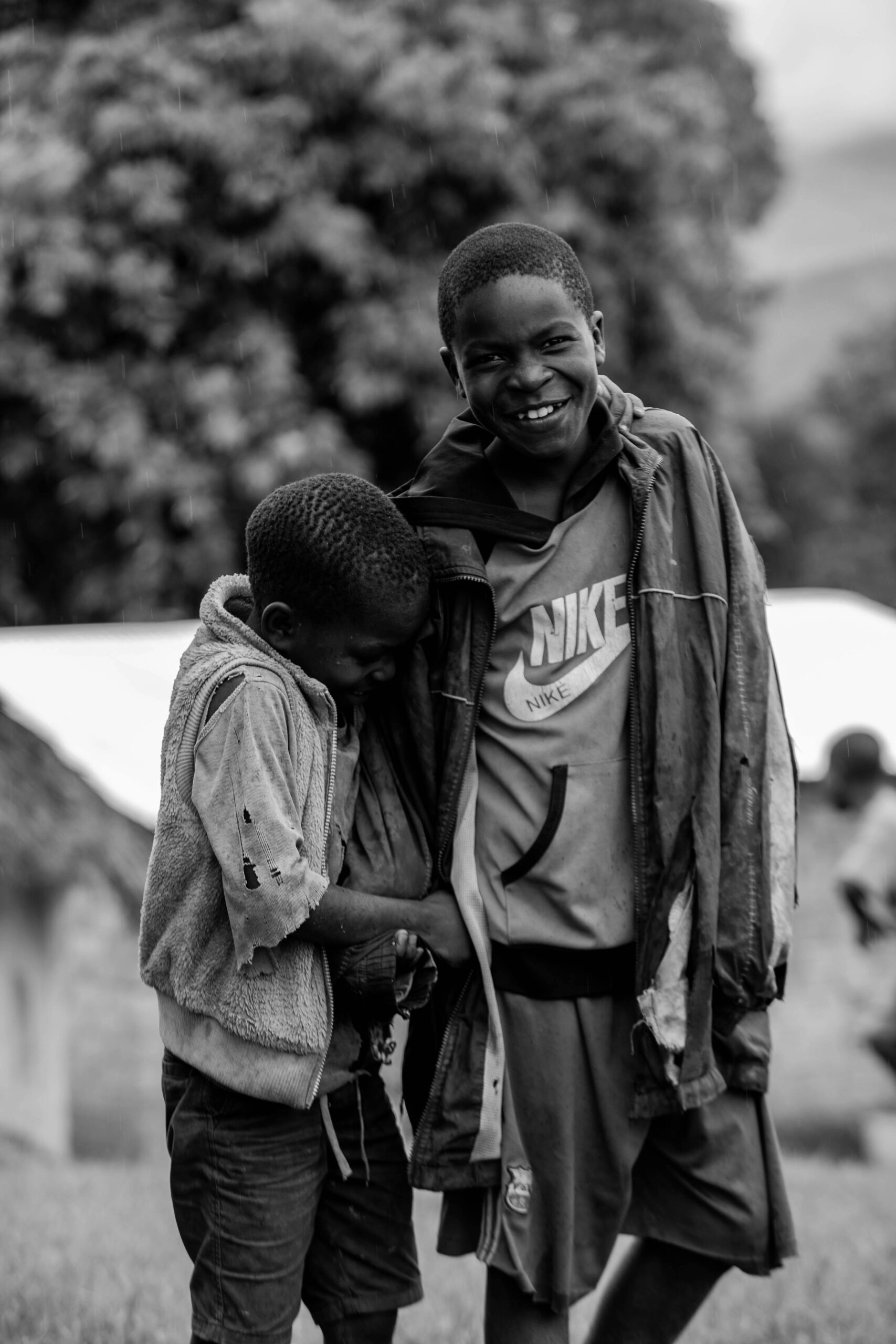 Black and white portrait of two African boys laughing outdoors in a village setting.