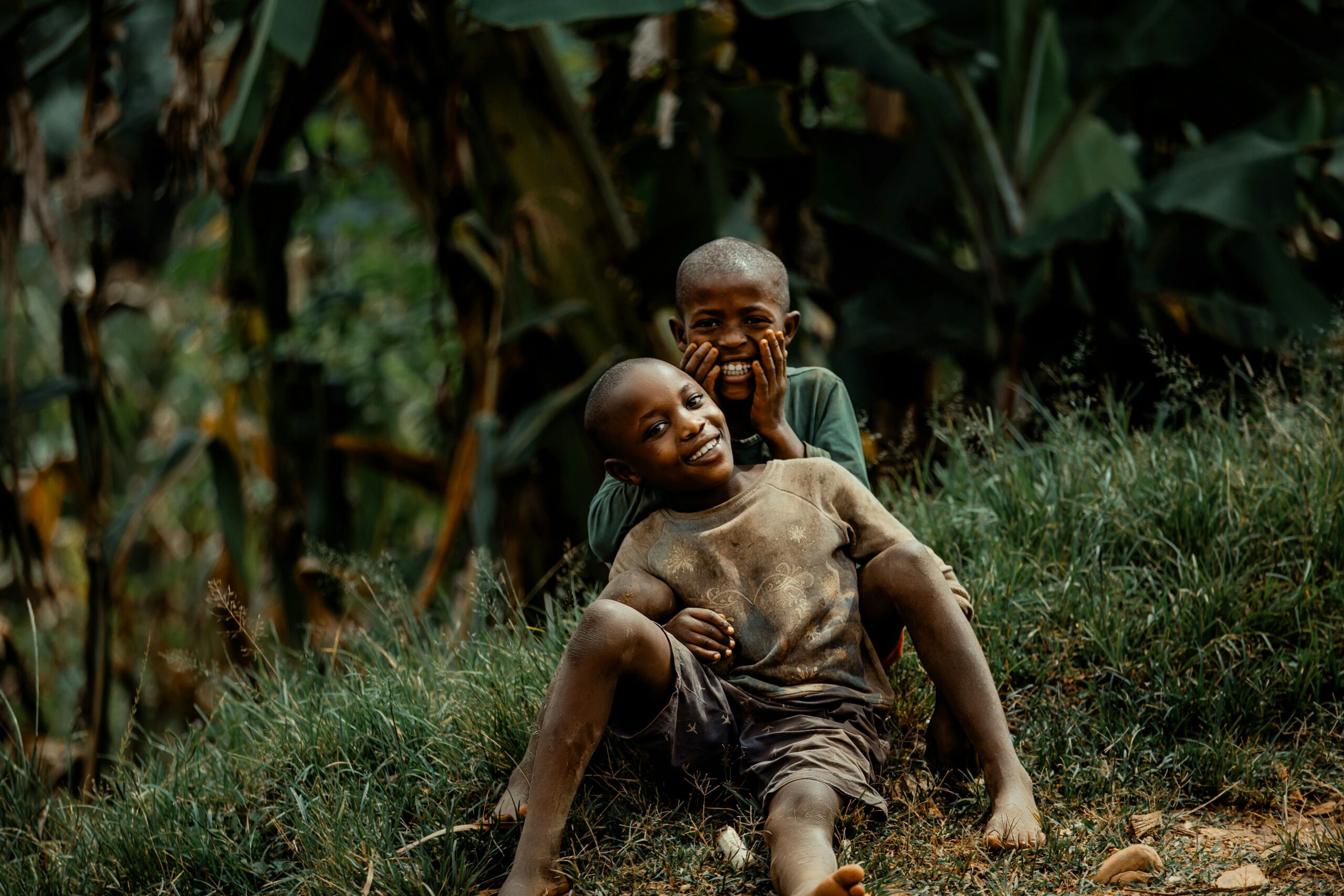Two happy children playing and laughing on a grassy hill, surrounded by lush greenery.