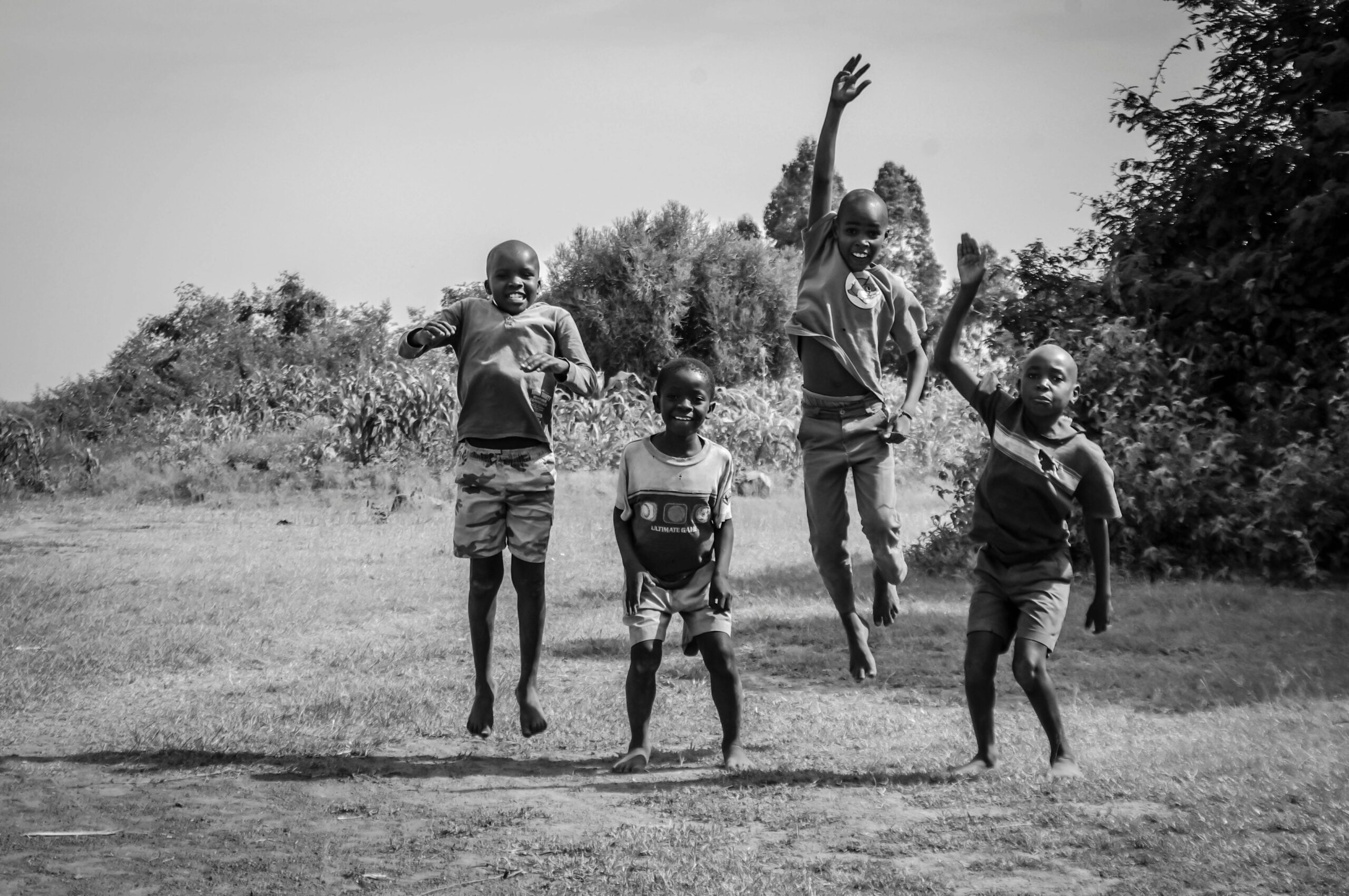 Black and white photo of four happy African boys joyfully jumping outside in Kisumu, Kenya.